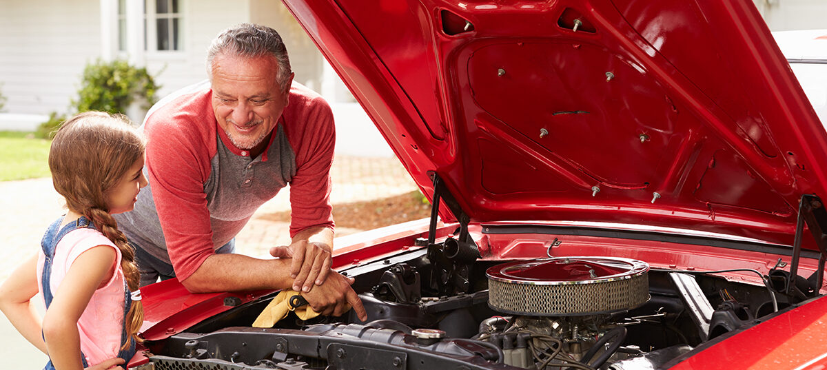a man showing a young girl what the red car looks like under the hood
