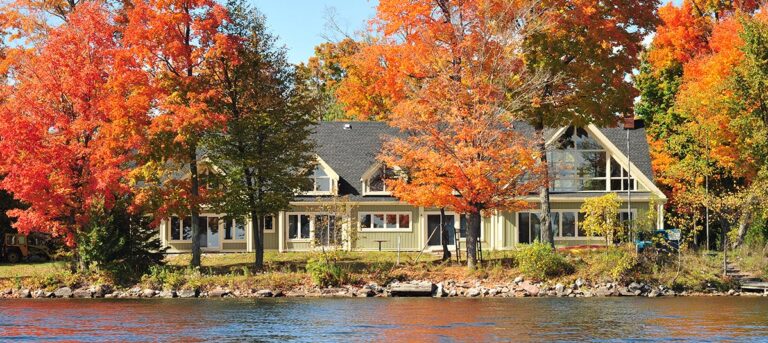 cottage sitting on the edge of a lake, surrounded by fall trees
