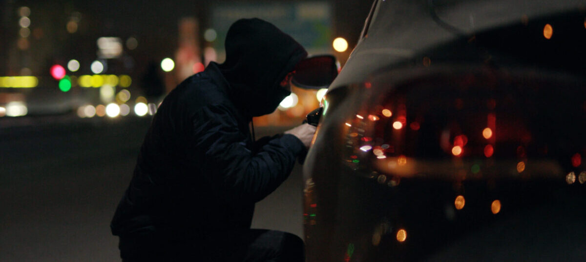 A car thief kneeling next to a target vehicle