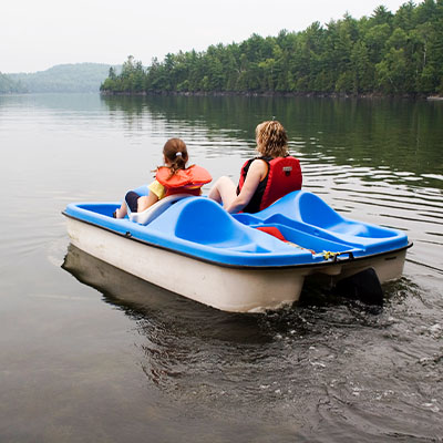Two teens wearing life jackets, in a paddle boat on a lake.