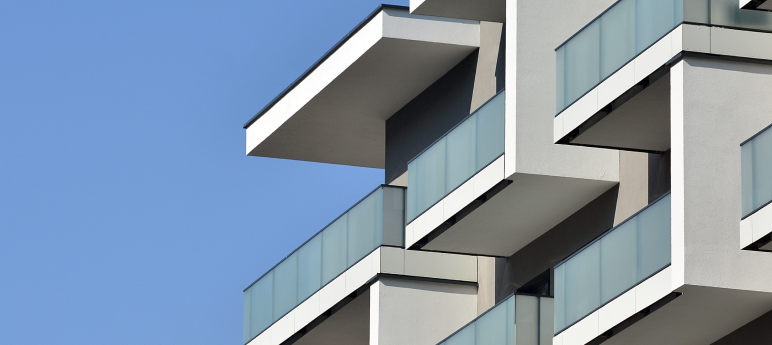 Modern apartment building facade with geometric balconies and glass railings against a clear blue sky.