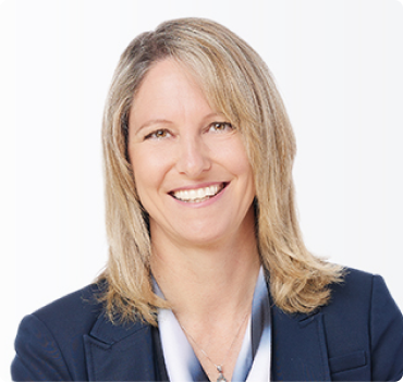 Professional headshot of a smiling woman with shoulder-length blonde hair, wearing a dark blazer and a light-colored blouse, against a plain white background.