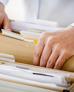 An office worker retrieving a manila folder out of a cabinet.