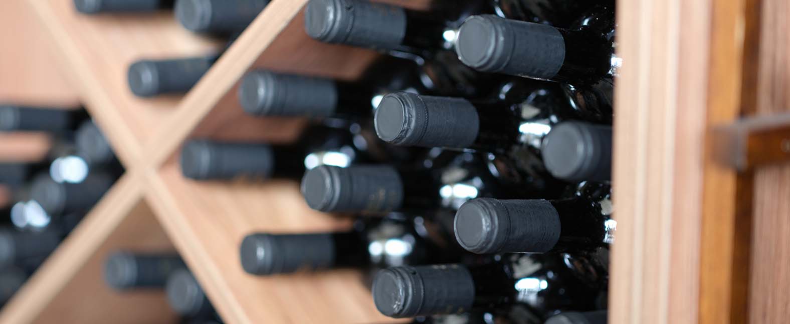 Various wine bottles are stacked on wooden racks.