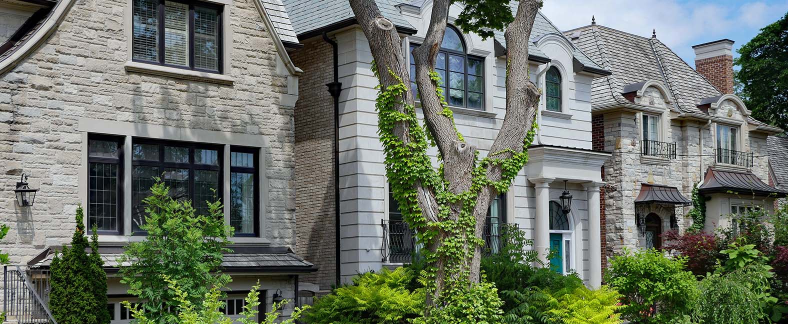 A row of single residential family homes; stone faces and greenery in front.