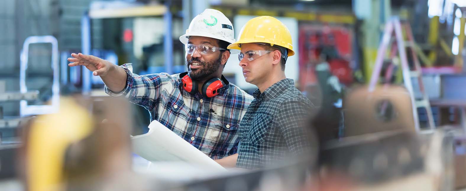 Two male workers wearing hard hats overlooking production in a manufacturing plant.