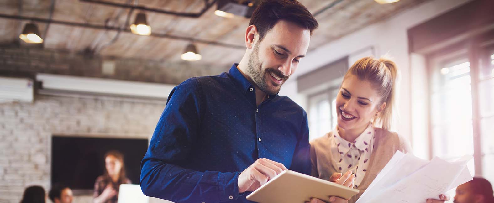 Two office workers looking over notes on a tablet.