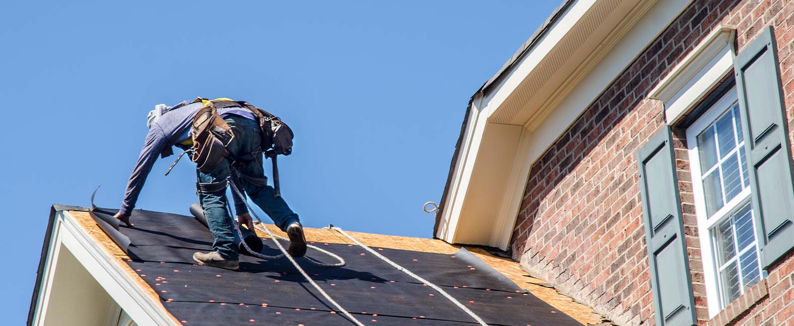 A roofer replacing shingles on a brick home.