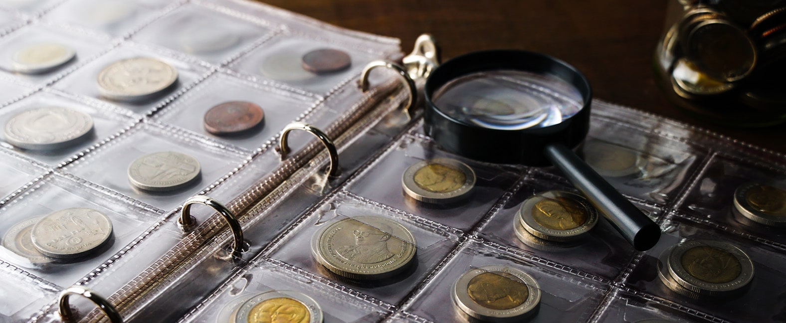 A magnifying glass sitting on a album of collector coins.