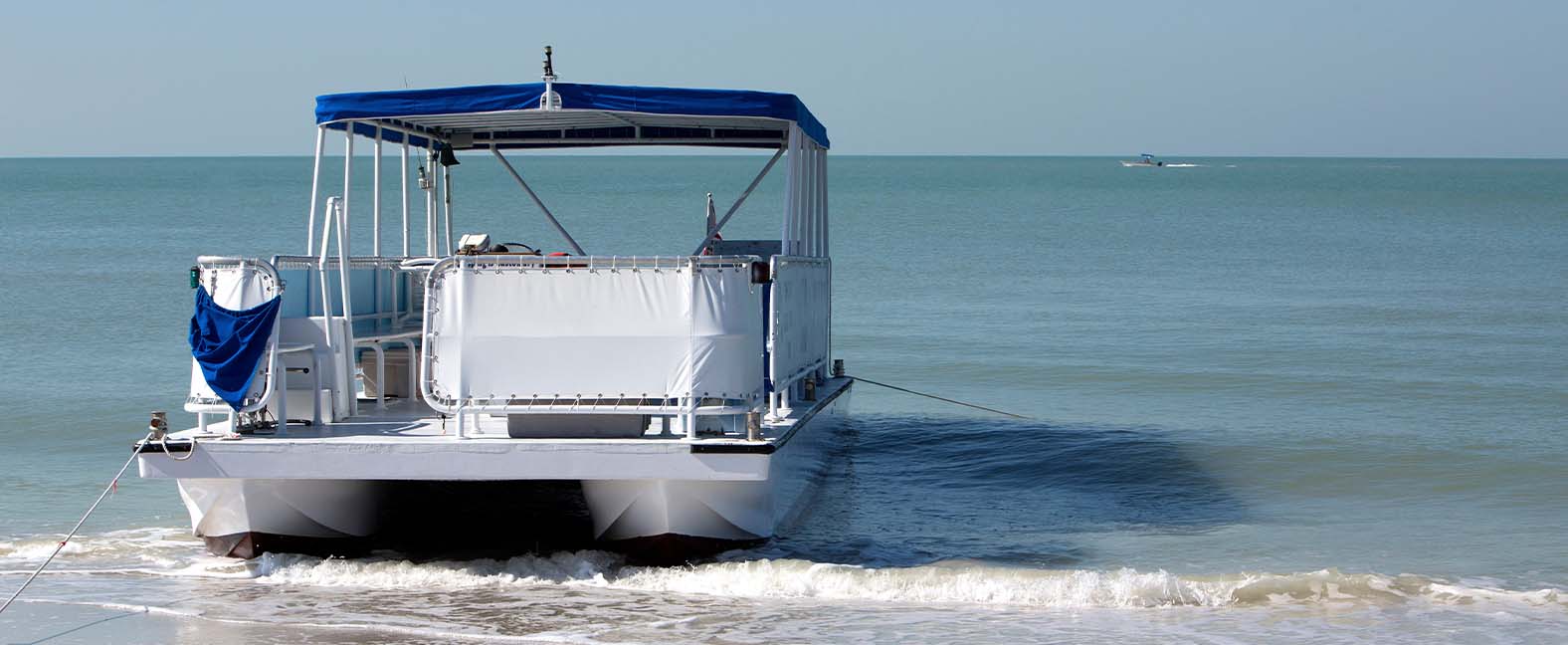 A mid-sized pontoon boat sitting on a shore.