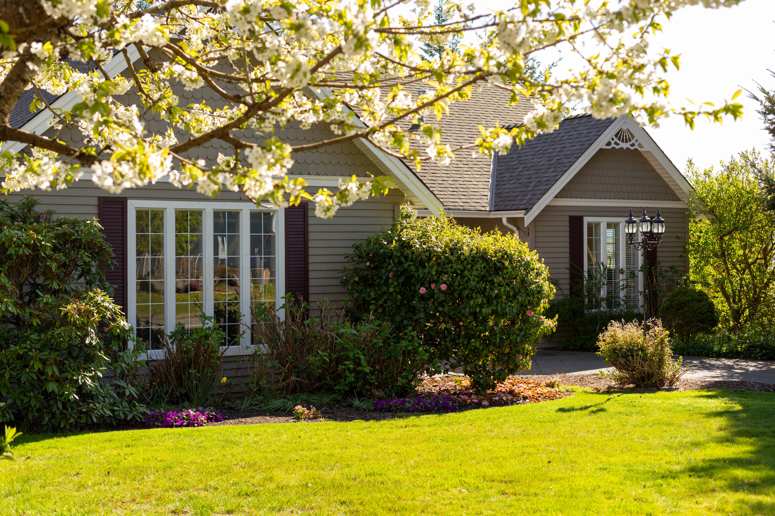 A charming house surrounded by blooming flowers and green grass, symbolizing the importance of spring home maintenance for a safe and inviting living space.